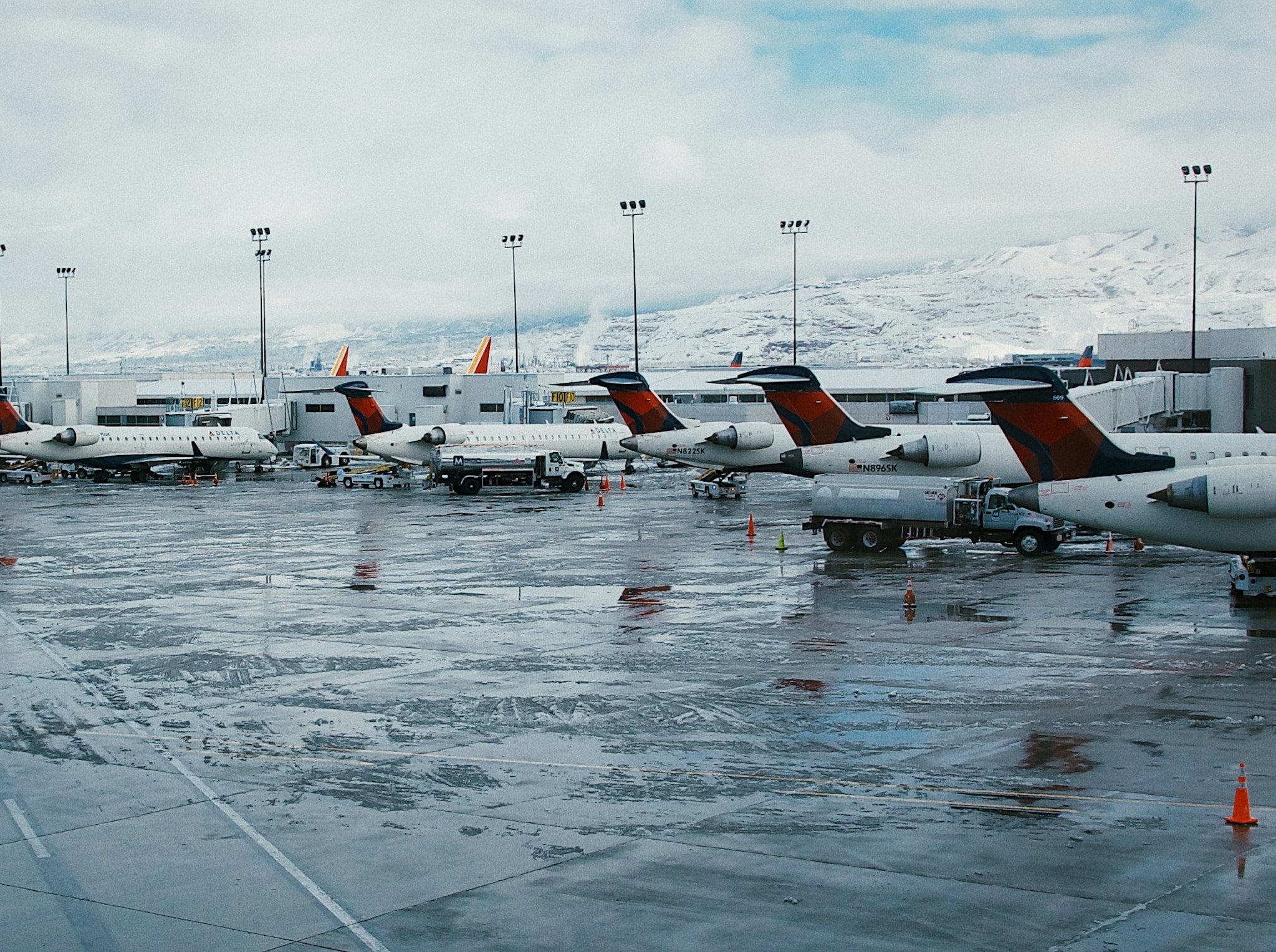 A row of regional jets parked at their gates on a wet apron, with snow-covered mountains behind